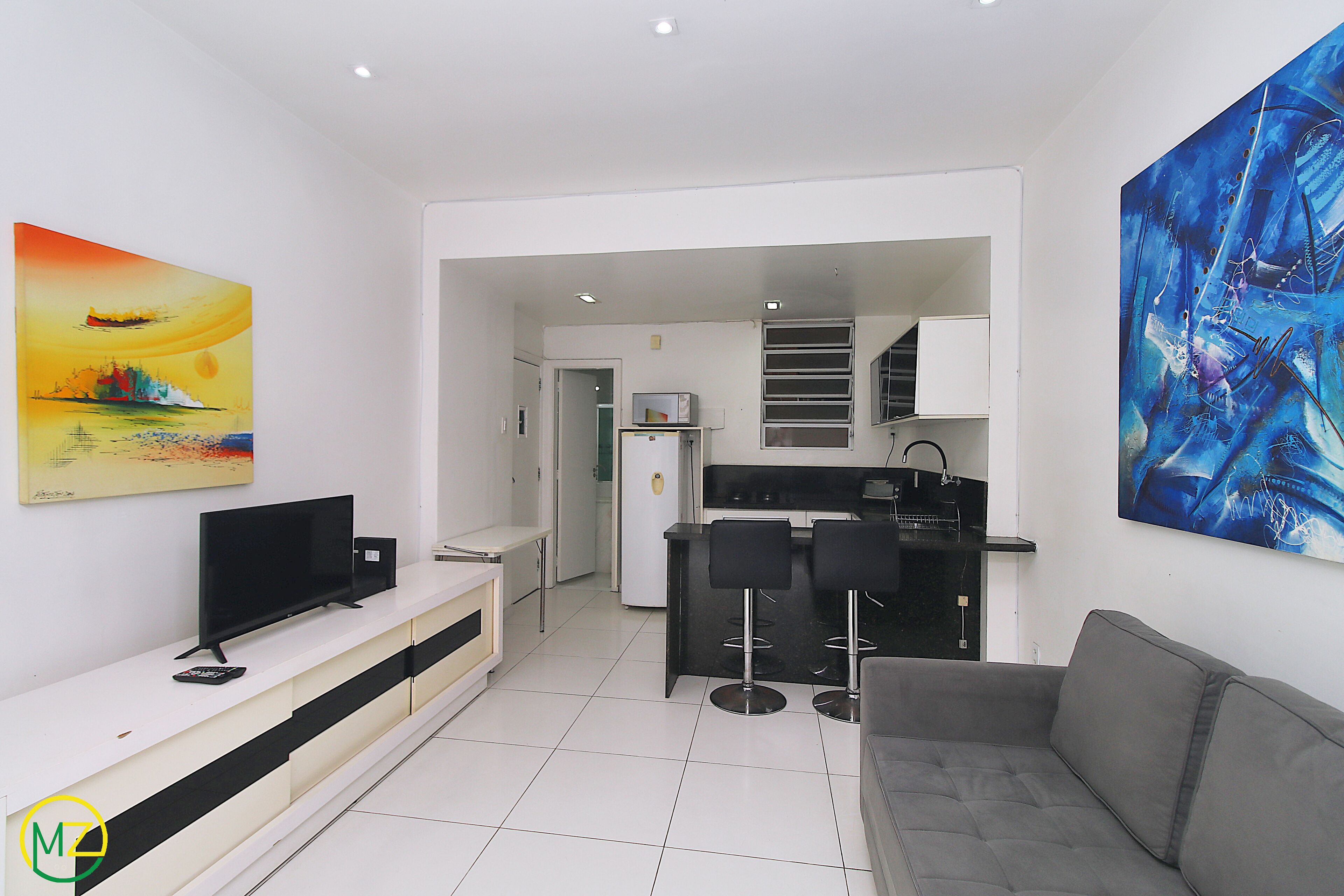 Ein modernes Wohnzimmer mit grauem Sofa, einem Flachbildfernseher und einem Essbereich mit einer schwarzen Bar und zwei schwarzen Barhocker.