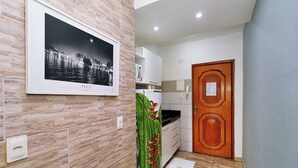Een moderne keuken met witte kasten, een magnetron en een koelkast. Op de muur hangt een lijst met een afbeelding van Parijs, en er is een houten deur met een decoratief patroon.