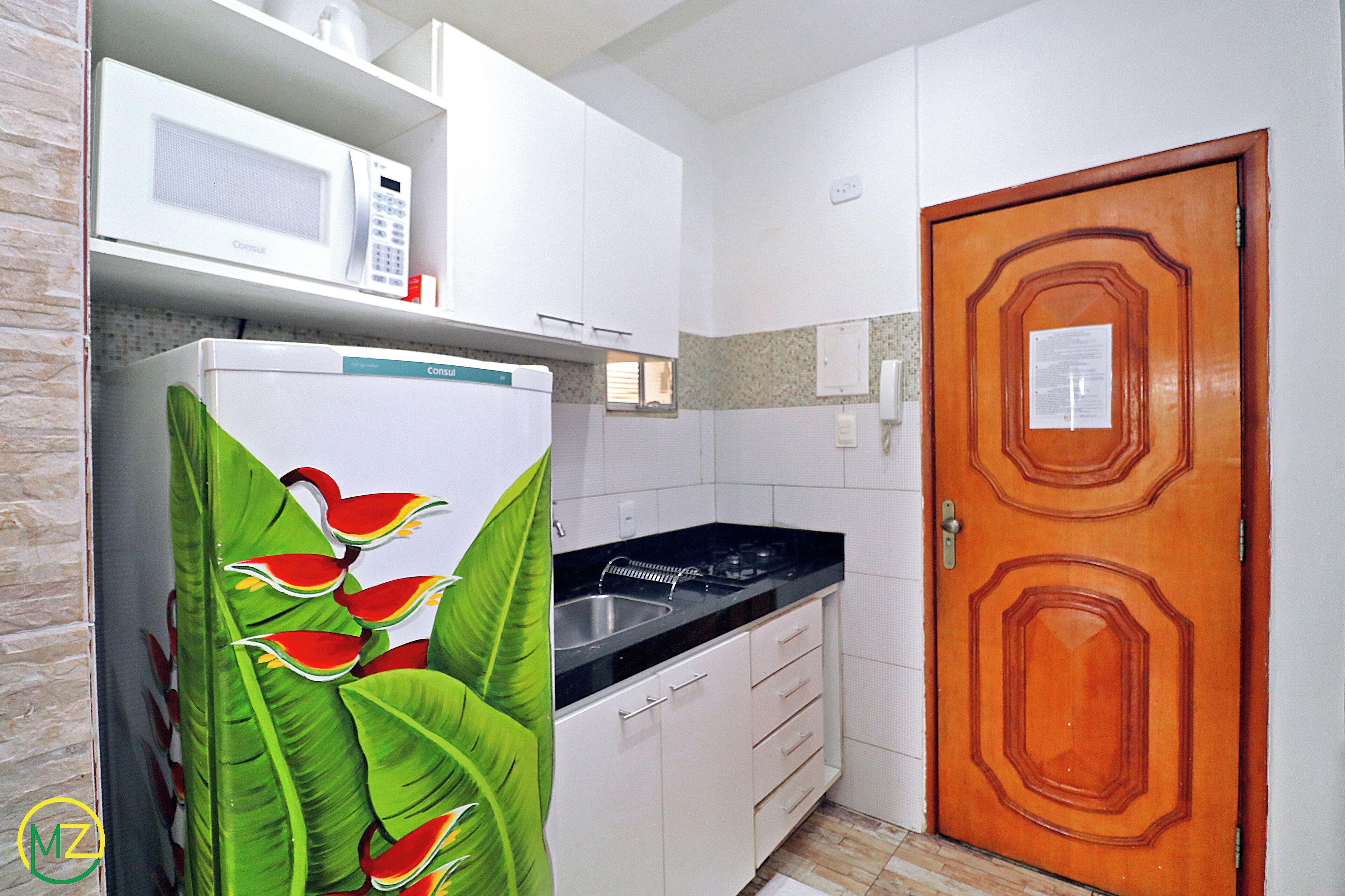 A kitchen with white cabinets, a microwave, a refrigerator with a tropical design, a black countertop, and a wooden door.
