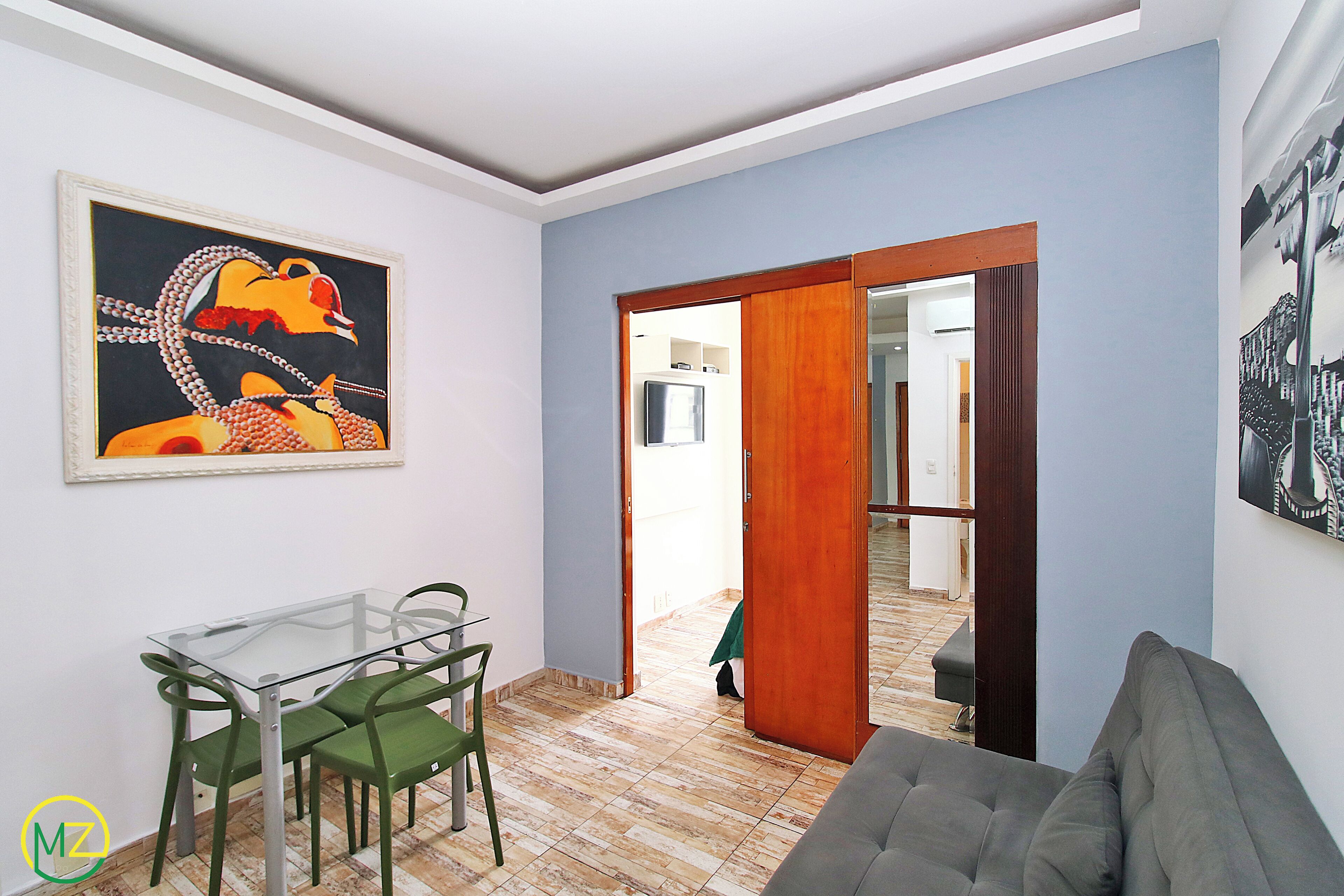 Una sala de estar con una mesa de vidrio, sillas verdes, un sofá gris y un cuadro en la pared.