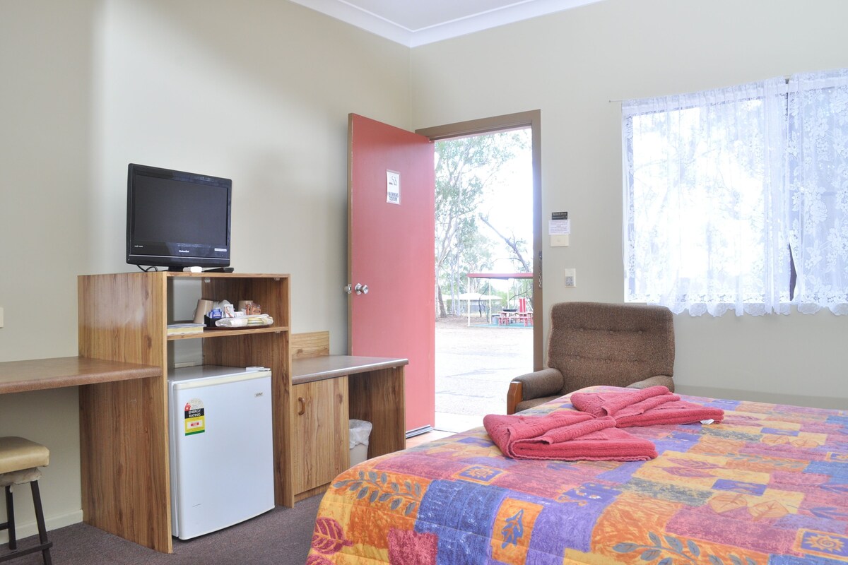 Una habitación con cama, escritorio, silla, televisor y refrigerador.