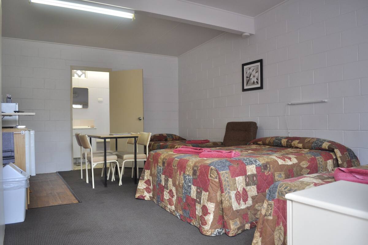 Een kleine, schone kamer met een bed, een bureau en een stoel. Er is ook een klein tafeltje en een afvalbak.