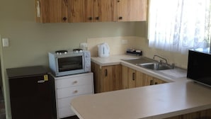 Une cuisine compacte dotée de meubles en bois, d’un four à micro-ondes, d’une bouilloire, d’un évier et d’un petit réfrigérateur.