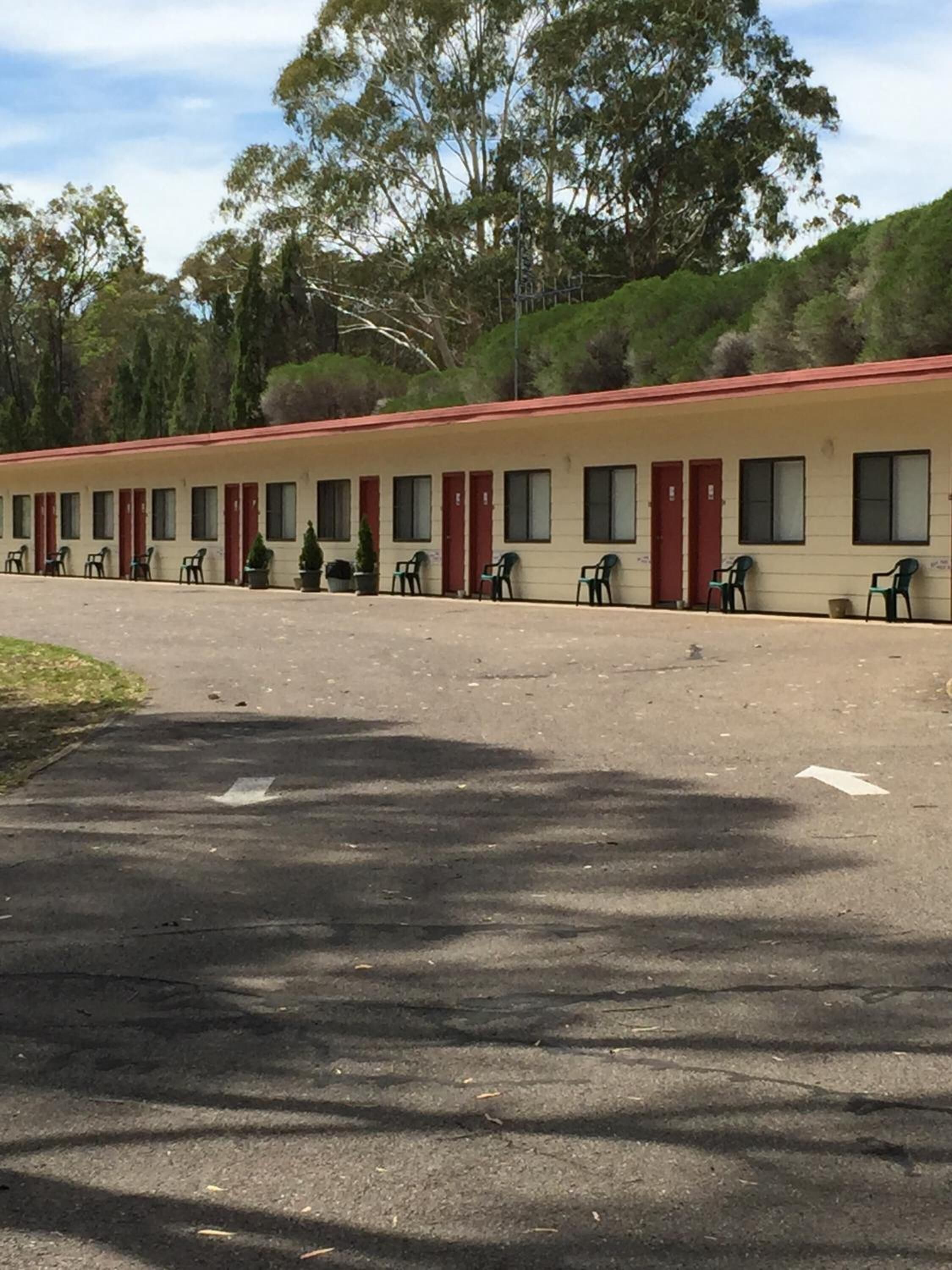 Un motel comprenant plusieurs chambres, chacune dotée d’une porte et de fenêtres. Il y a des chaises à l’extérieur et un petit espace aménagé en jardin.