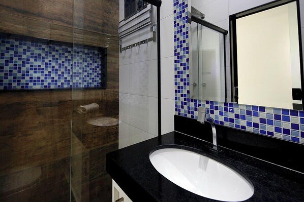 A modern bathroom with a black countertop, a white sink, and a glass shower enclosure.