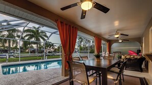 Un espace aménagé au bord de la piscine, comprenant une table à manger, des chaises et des ventilateurs de plafond.