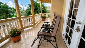 A balcony with a white balustrade, a table with chairs, potted plants, and a door with a window. - DIY Vacation Home (Laborie)