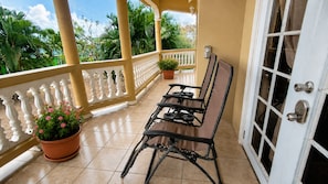 A balcony with a white balustrade, a table with chairs, potted plants, and a door with a window.
