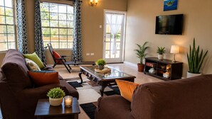A living room with a sofa, armchair, coffee table, and a TV mounted on the wall. - DIY Vacation Home (Laborie)
