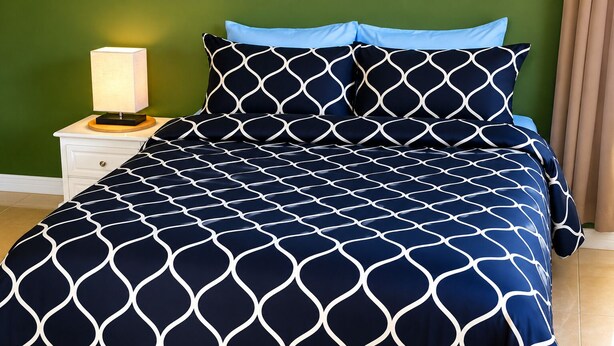 A bed with a geometric patterned bedspread, a bedside lamp, and a nightstand with a drawer. - DIY Vacation Home (Laborie)