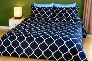 Ein Bett mit geometrischem Muster auf der Tagesdecke, eine Nachttischlampe und ein Nachttisch mit Schublade.