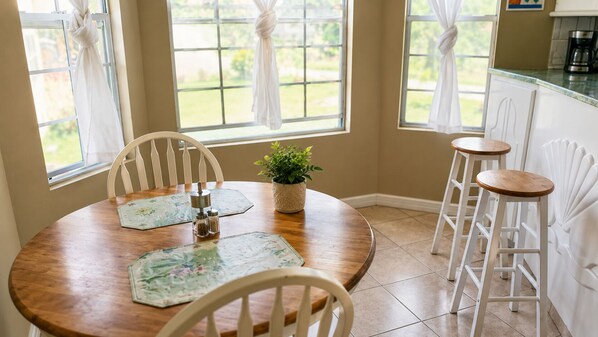 A dining area with a round wooden table, white chairs, and a potted plant.