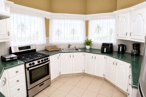 A kitchen with white cabinets, a stove, a sink, and a coffee maker.