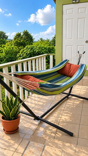 A hammock chair with a striped cushion, a potted plant, and a white door in the background.