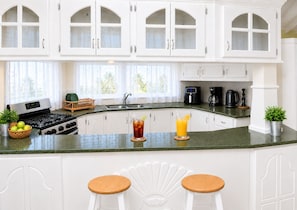 A kitchen with white cabinets, a gas stove, a coffee maker, and two stools.
