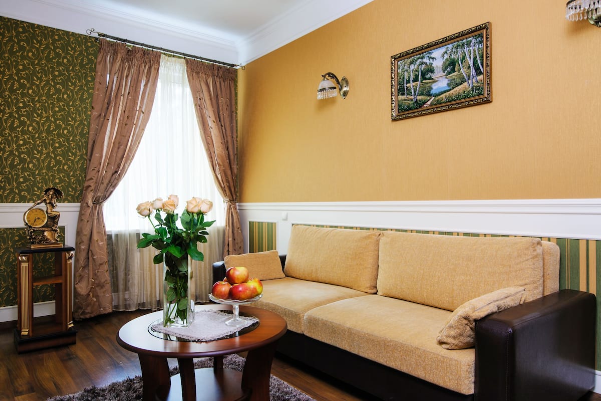 Ein Wohnzimmer mit einer Couch, einem Couchtisch mit Äpfeln und Rosen, einer Uhr und einem Bild an der Wand.