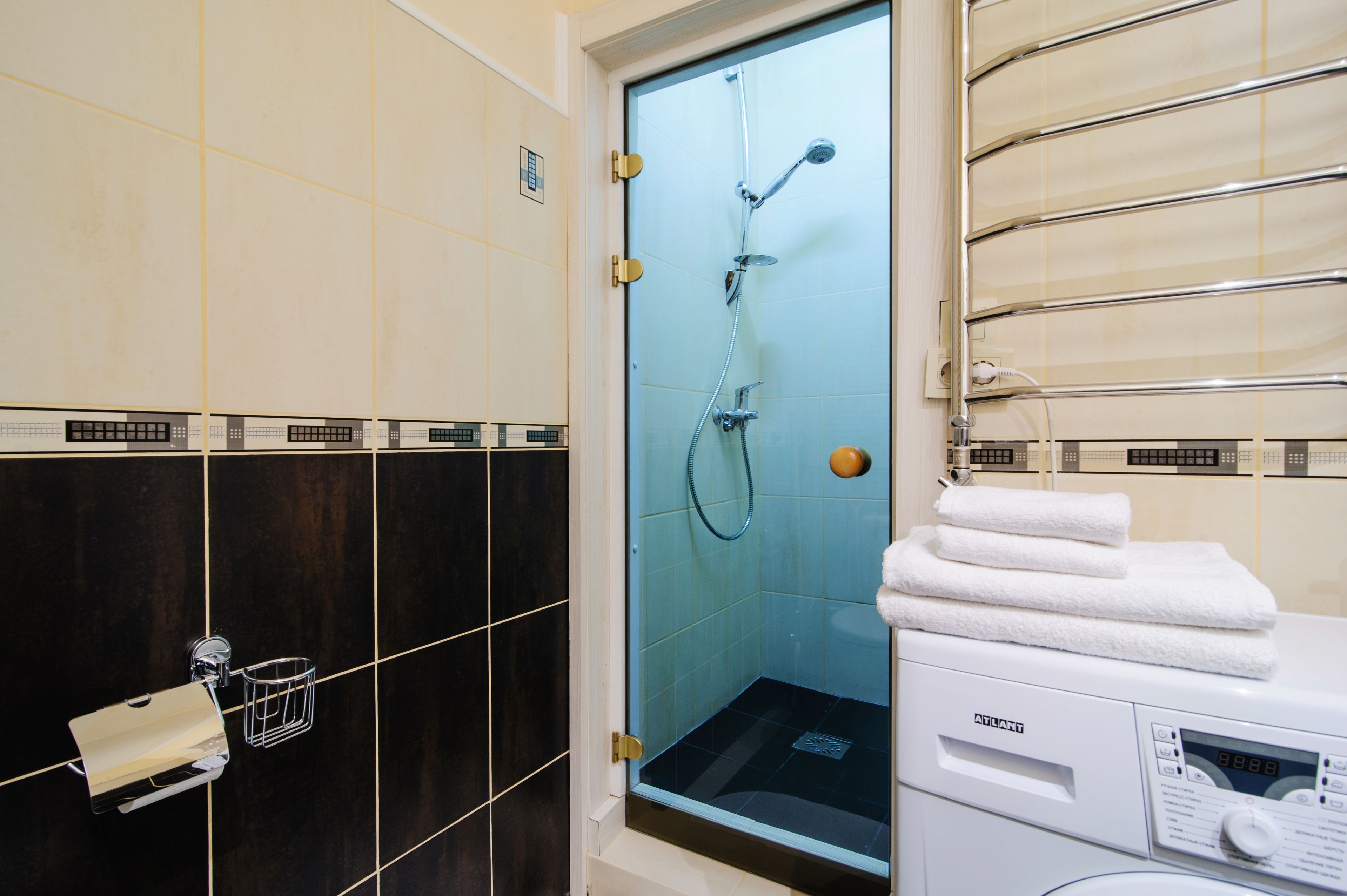 A bathroom with a glass-enclosed shower, a white washing machine, and a towel rack with folded towels.