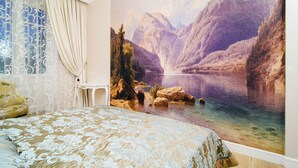 Een slaapkamer met een groot muurschildering van een bergmeer, een bed met een bloemenbedekking en een raam met gordijnen.