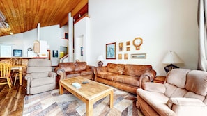 A spacious living room with a wooden ceiling, a wooden coffee table, two leather sofas, a beige armchair, and a patterned rug. - Snowcreek Resort Vacation Rental 554 (Mammoth Lakes)