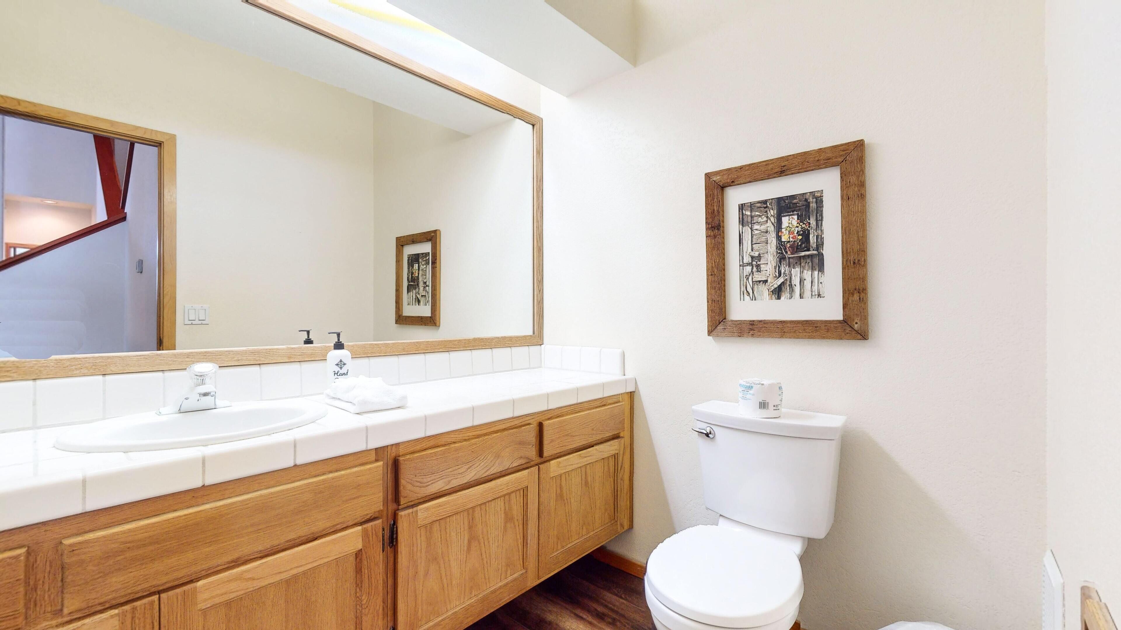 Un baño con tocador de madera, dos lavamanos, inodoro y un espejo grande.