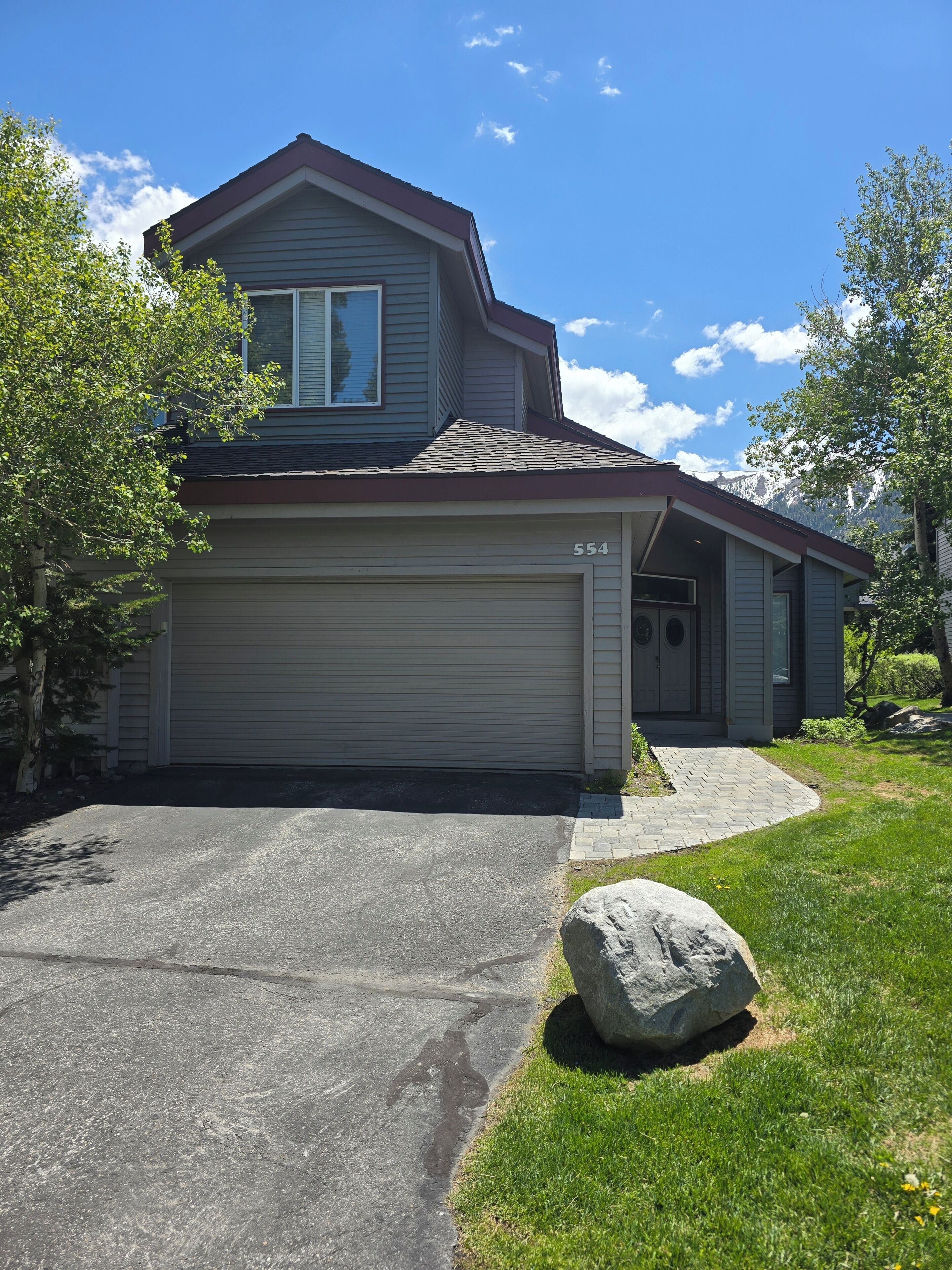 A residential house with a garage, a driveway, and a large rock in the front yard.