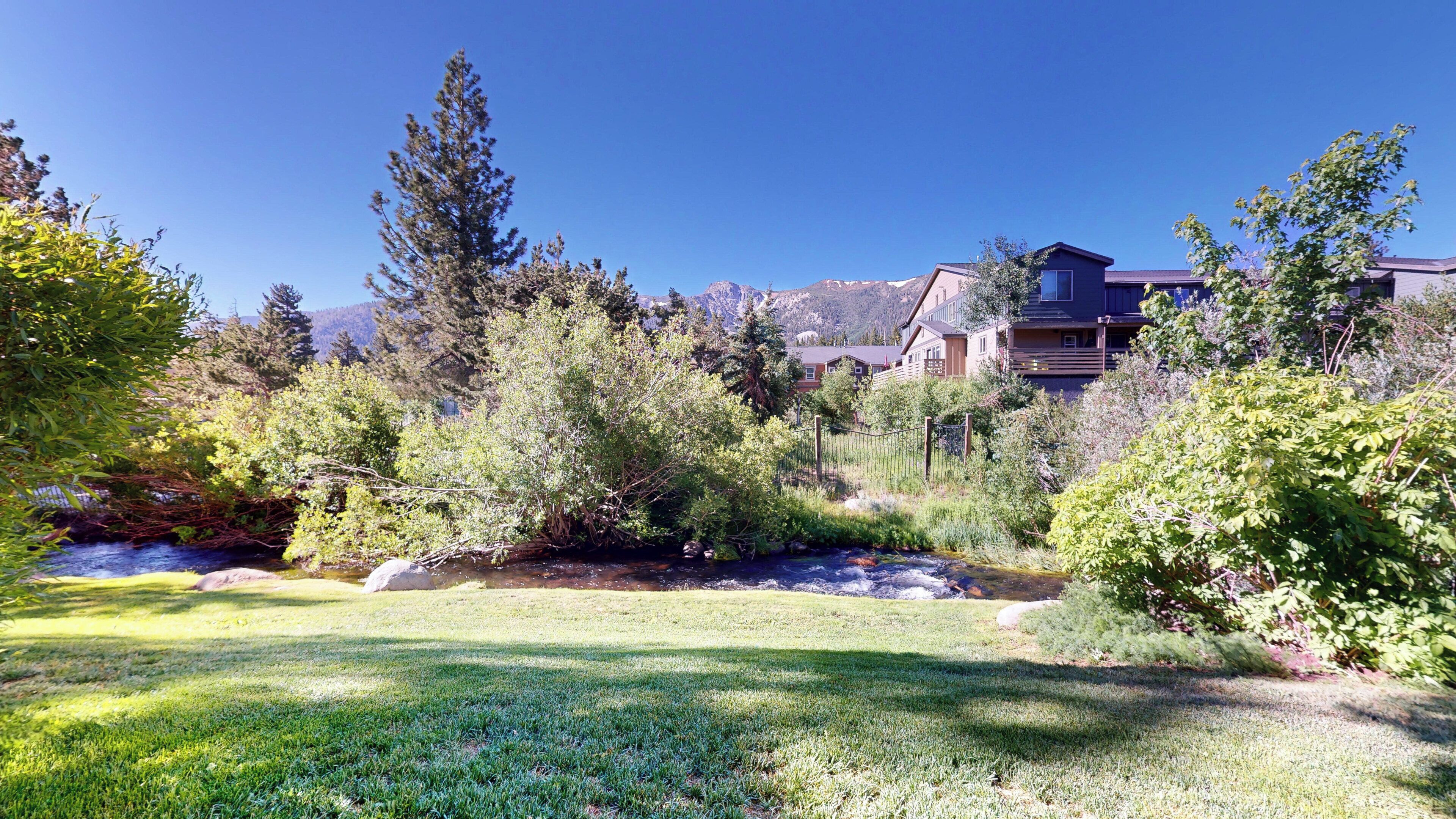 Un quartier résidentiel avec une pelouse verdoyante, un petit ruisseau et des maisons adossées à un paysage montagneux.