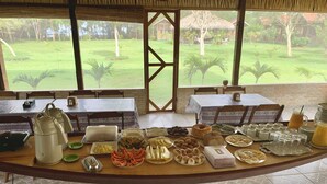 A breakfast buffet with various food items and beverages, set against a backdrop of a lush garden and a view of a building with a red roof. - Alta Vista Amazon Lodge (Manacapuru)
