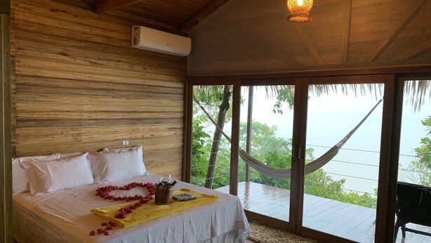 A bedroom with a wooden ceiling, a bed with white linens, a hammock outside the window, and a view of greenery. - Alta Vista Amazon Lodge (Manacapuru)