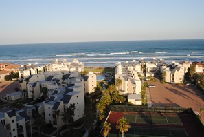 Zona residencial costera con edificios modernos, una cancha de tenis y vista al océano.