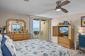 Un dormitorio con una cama grande, un ventilador de techo, un televisor y vista al océano a través de un ventanal corredizo.