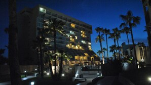 A multi-story hotel with balconies, palm trees, and a well-lit entrance area. - Beachfront and Gorgeous Sunrise Views - A Beach Lover's Paradise  (South Padre Island)