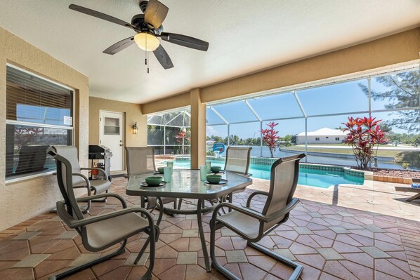 A covered patio area with a table and chairs, a ceiling fan, and a view of a swimming pool. - Great Water views! Southern Exposure Pool, Pet-Friendly- Villa On The Lake -Roelens Vacations (Cape Coral)