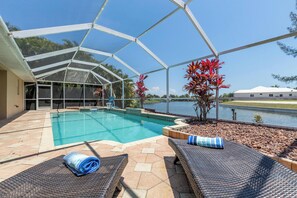 A covered swimming pool with lounge chairs and a view of a lake. - Great Water views! Southern Exposure Pool, Pet-Friendly- Villa On The Lake -Roelens Vacations (Cape Coral)