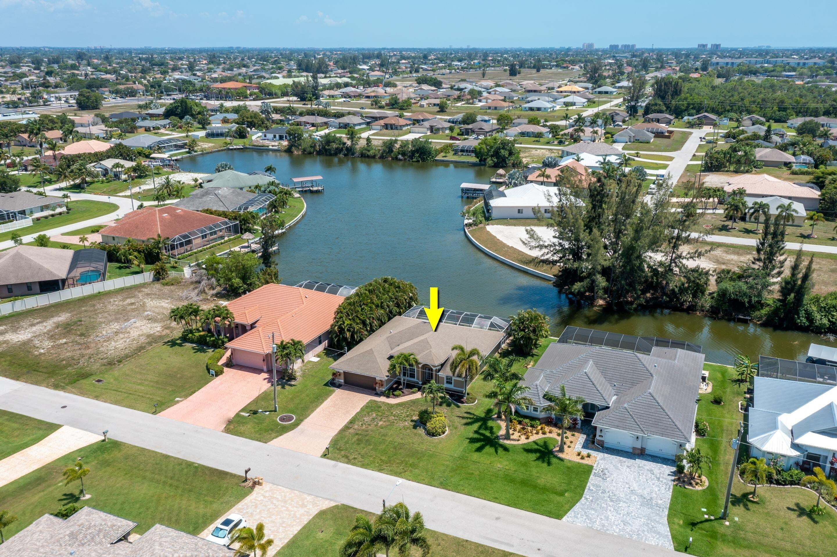 An aerial view of a residential area with houses, a lake, and a highlighted building with a large arrow.