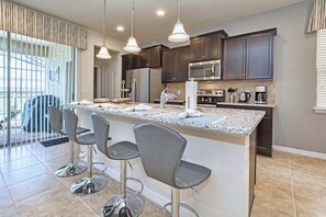A modern kitchen with dark cabinets, stainless steel appliances, and a central island with bar stools.