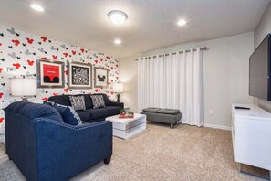 A living room with a black sofa, a blue armchair, a coffee table, and a flat-screen TV.