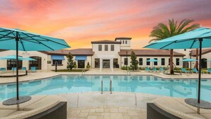 Una piscina con lettini e ombrelloni, un edificio con tetto in tegole e un cielo al tramonto.