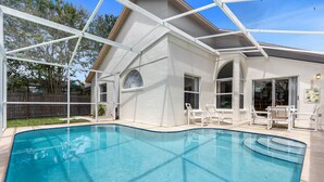 A swimming pool with a glass enclosure, surrounded by a house with large windows and a covered patio area. - 2974 3BD Family home + Pool (Kissimmee)