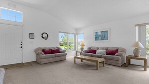 A living room with two beige sofas, a wooden coffee table, a white door, a window, and a framed picture on the wall. - 2974 3BD Family home + Pool (Kissimmee)
