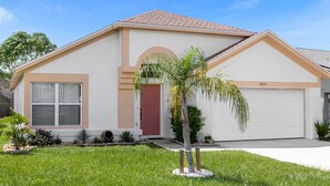 A single-story house with a red door, beige exterior, and a garage. - 2974 3BD Family home + Pool (Kissimmee)