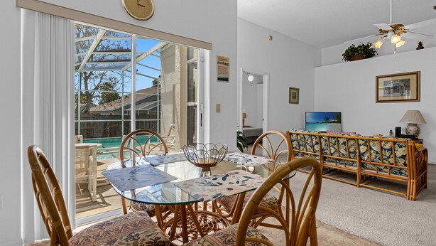 A dining area with a glass table and chairs, a sliding glass door leading to an outdoor pool, and a rattan sofa in the background. - 2974 3BD Family home + Pool (Kissimmee)