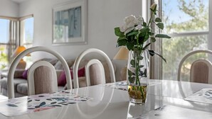 A dining table with a vase of white flowers, white chairs, and a window with a view of trees. - 2974 3BD Family home + Pool (Kissimmee)
