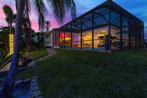 Een modern huis met een glazen patio, een zwembad en een verzorgd gazon.