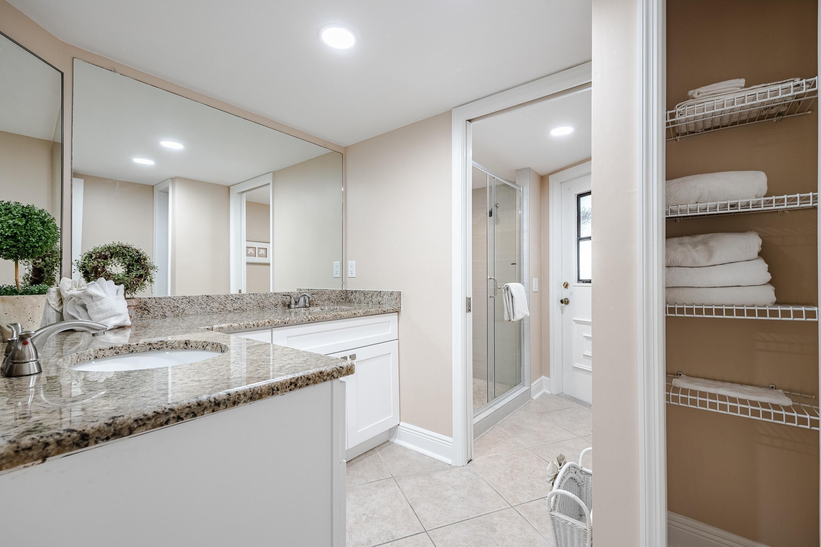A modern bathroom with a granite countertop sink, a large mirror, and a walk-in shower.