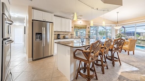 A spacious kitchen with a large island, stainless steel appliances, and a view of the outdoor pool area. - Boater's Delight | Gulf Access, Bikes, Kayaks, Pool Table, Heated Poo/Spa - Villa Blue Sky - Roelens (Cape Coral)