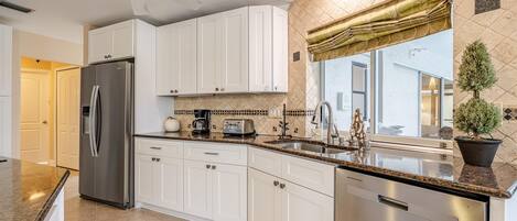 A modern kitchen with white cabinets, stainless steel appliances, and a granite countertop.