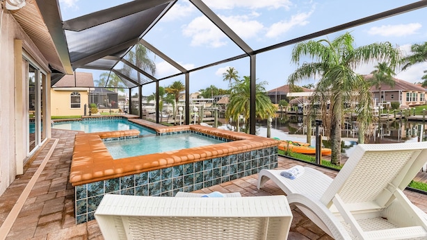 A covered swimming pool area with lounge chairs and a view of the surrounding neighborhood. - Boater's Delight | Gulf Access, Bikes, Kayaks, Pool Table, Heated Poo/Spa - Villa Blue Sky - Roelens (Cape Coral)