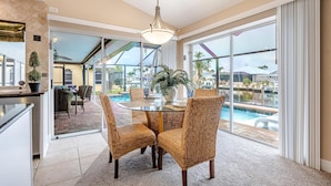A dining area with wicker chairs, a glass table, and a view of a swimming pool. - Boater's Delight | Gulf Access, Bikes, Kayaks, Pool Table, Heated Poo/Spa - Villa Blue Sky - Roelens (Cape Coral)