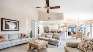 A spacious living room with a large sofa, a coffee table, and a ceiling fan. There is a dining area with a table and chairs visible in the background. - Boater's Delight | Gulf Access, Bikes, Kayaks, Pool Table, Heated Poo/Spa - Villa Blue Sky - Roelens (Cape Coral)