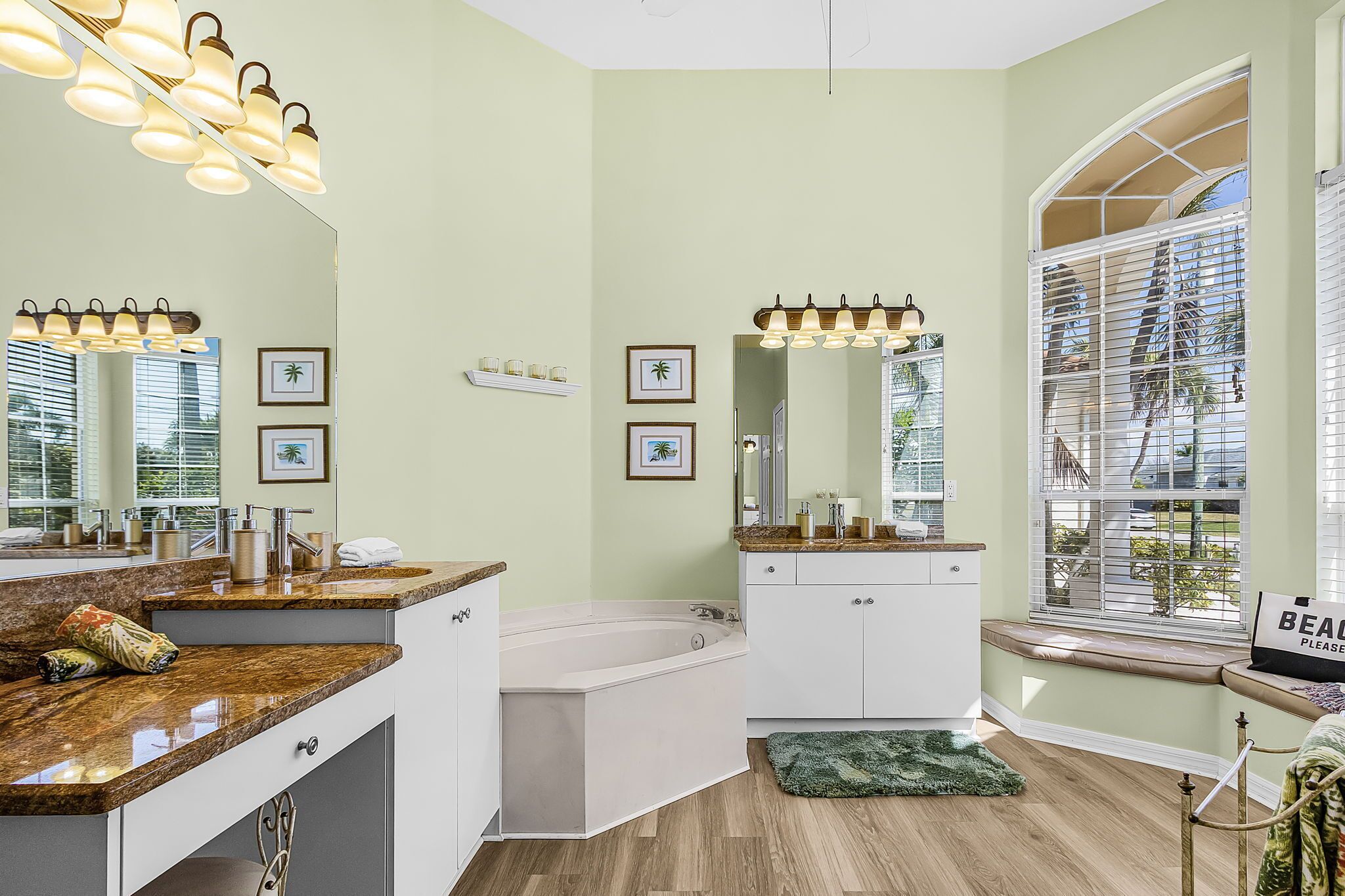 Une salle de bain avec une baignoire, un meuble-lavabo avec un miroir et une fenêtre donnant sur des palmiers.